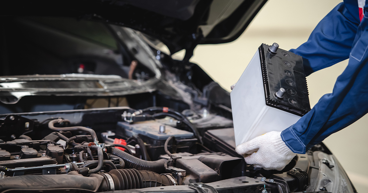 A close-up of a service technician placing a battery into a vehicle's engine