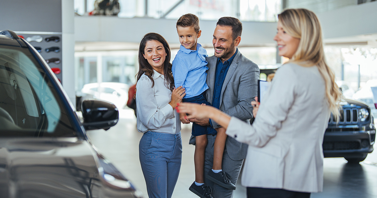 A family with a car salesperson in the dealership looking at a vehicle.